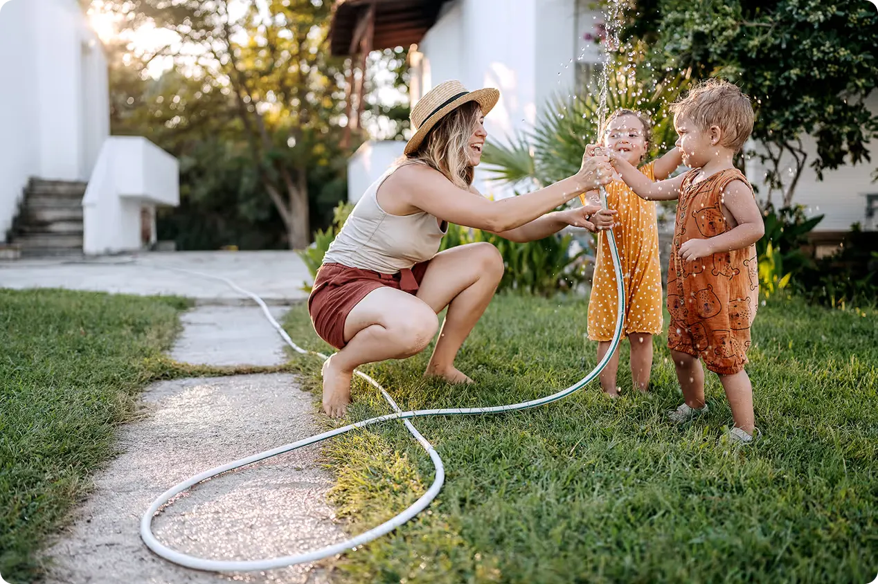 A parent playing with a garden hose with two young children